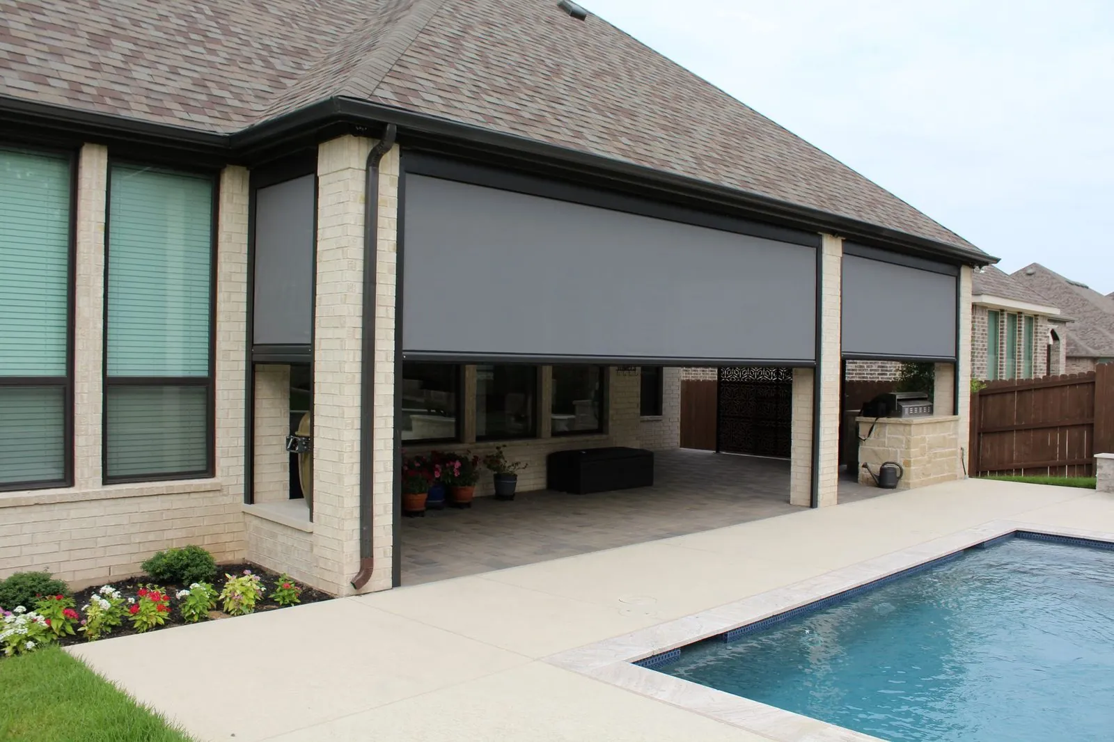 Two motorized solar screens lowered over a brick patio next to a pool