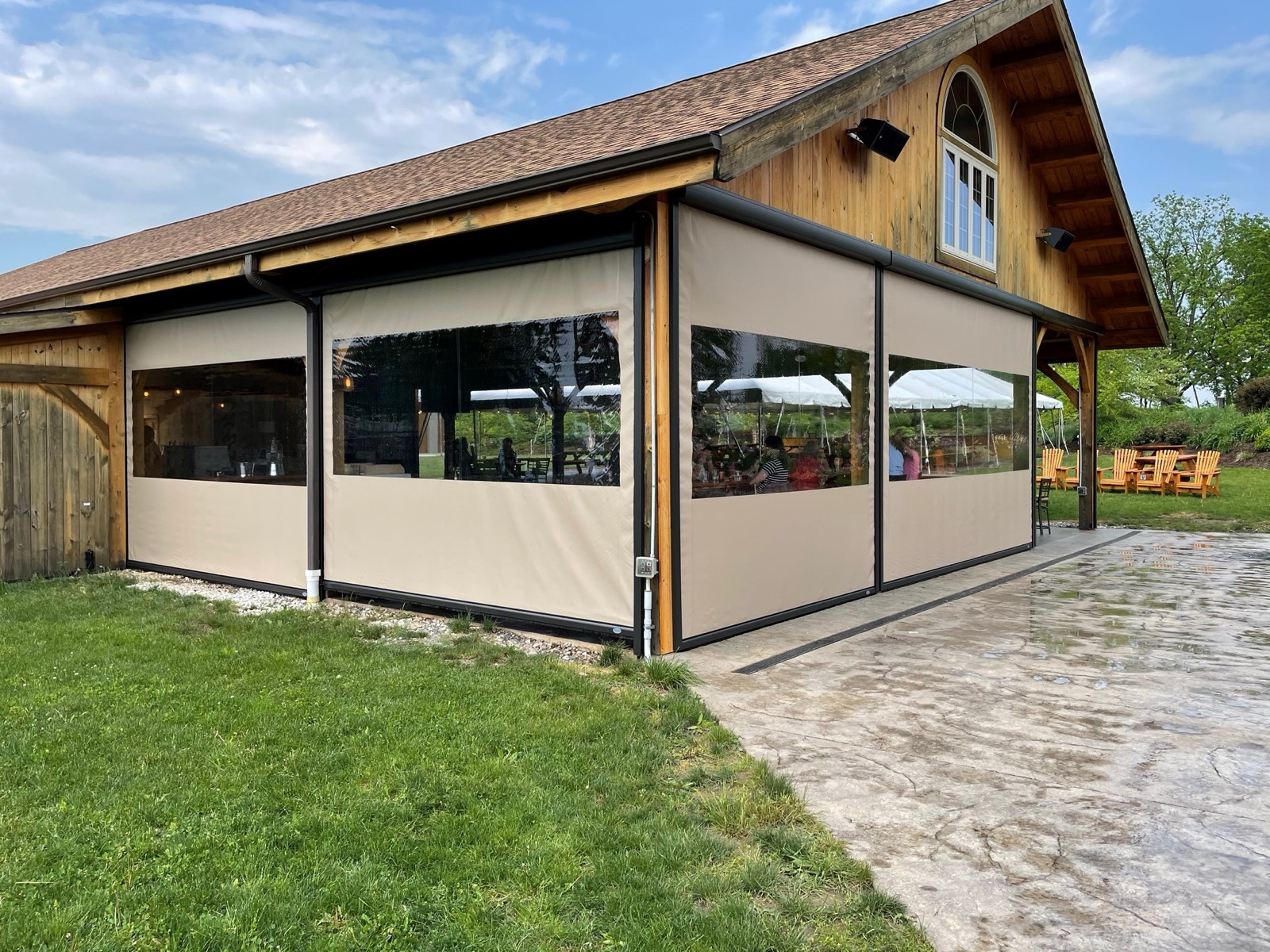 Clear vinyl motorized screens lowered across the open sides of a timber-frame pavilion, a MagnaTrack dealer network installation